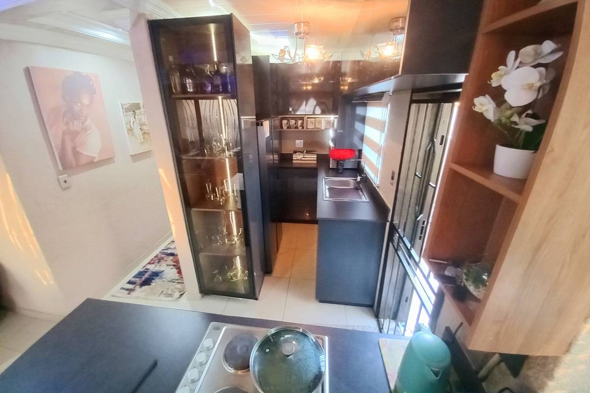 A compact, modern kitchen featuring dark cabinetry, integrated hob, stainless steel sink, and built-in display shelving, offering a functional and stylish cooking space.