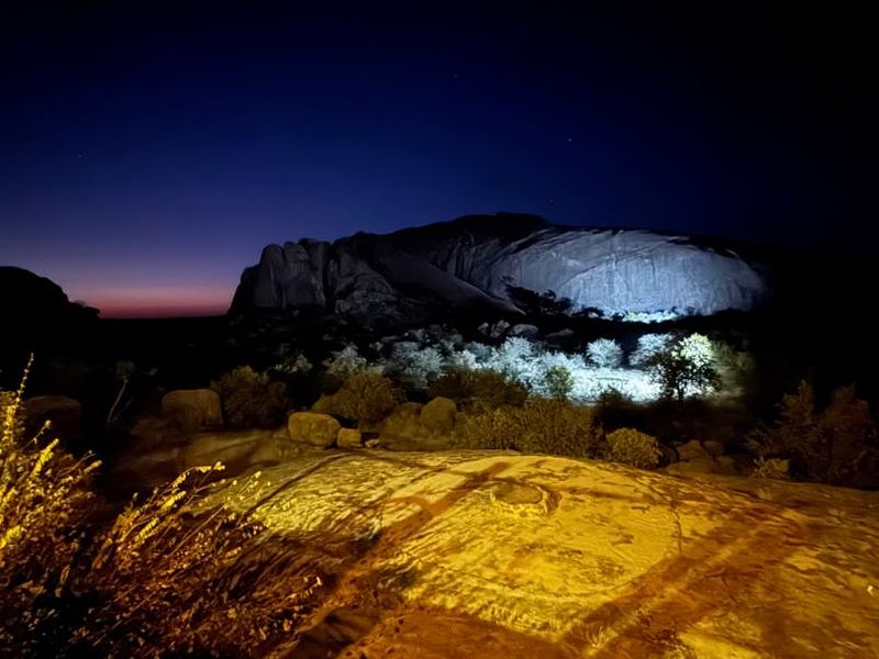 A night view of the lodge's natural surroundings, featuring illuminated rock formations and indigenous landscape under a twilight sky.