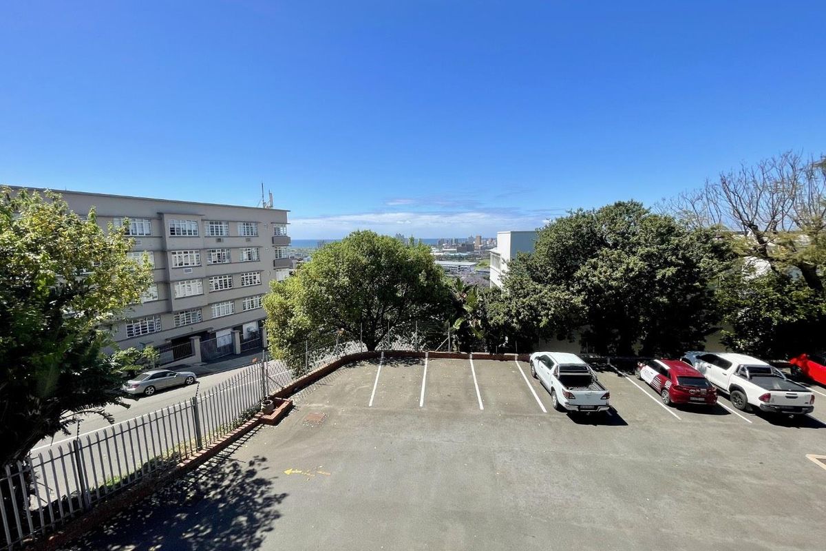 An elevated view of the property's rear asphalt parking area, featuring marked parking bays and perimeter metal fencing with surrounding trees.