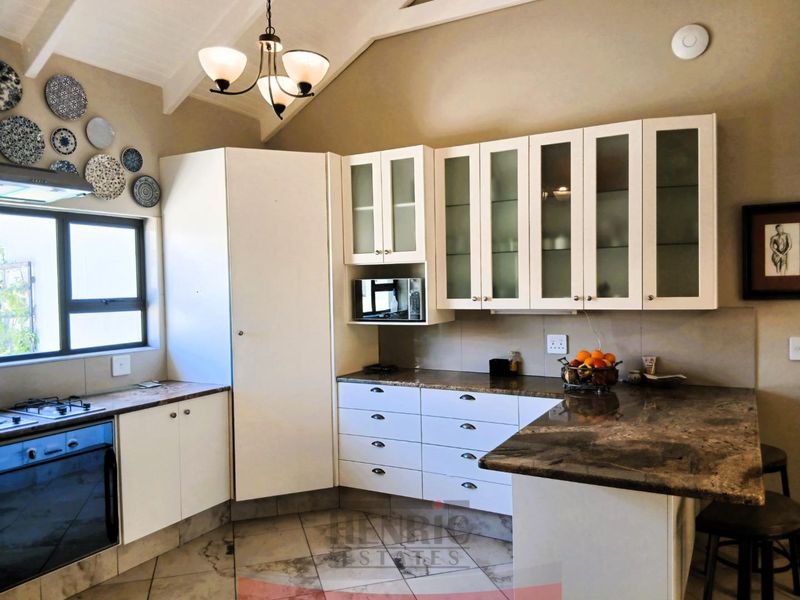 A well-maintained kitchen featuring white cabinetry, granite countertops, built-in appliances, and a vaulted ceiling with a feature chandelier.