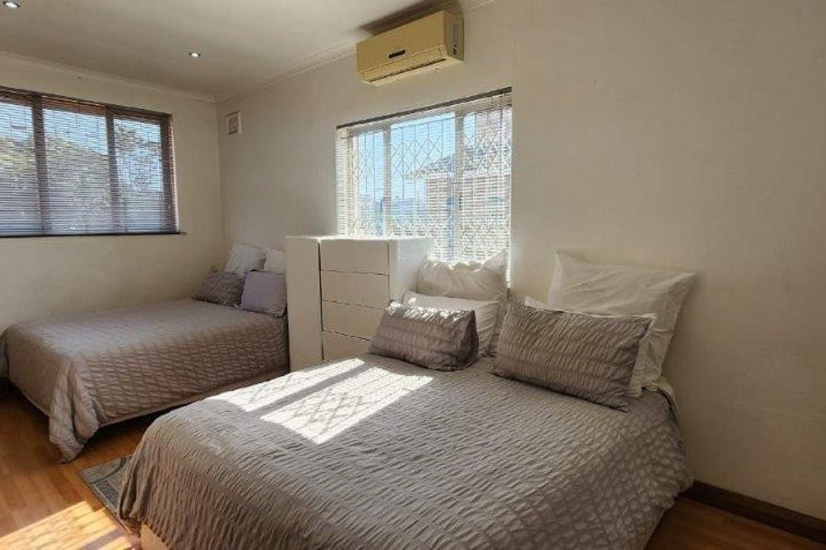 A functional bedroom featuring laminate flooring, built-in cupboards, recessed lighting, and a wall-mounted air conditioning unit.