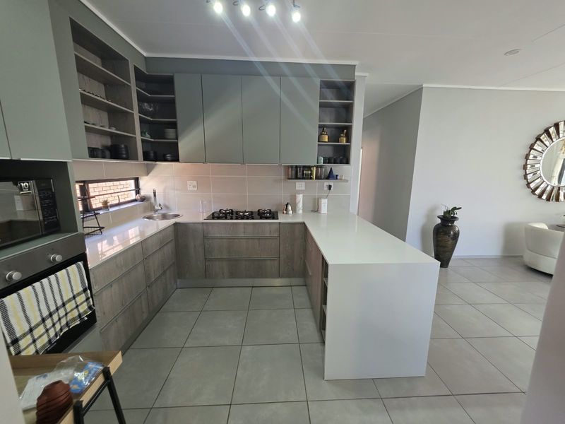 Modern kitchen featuring sleek two-tone cabinetry, stone countertops, a gas hob, built-in oven, and a functional breakfast bar with tiled flooring.