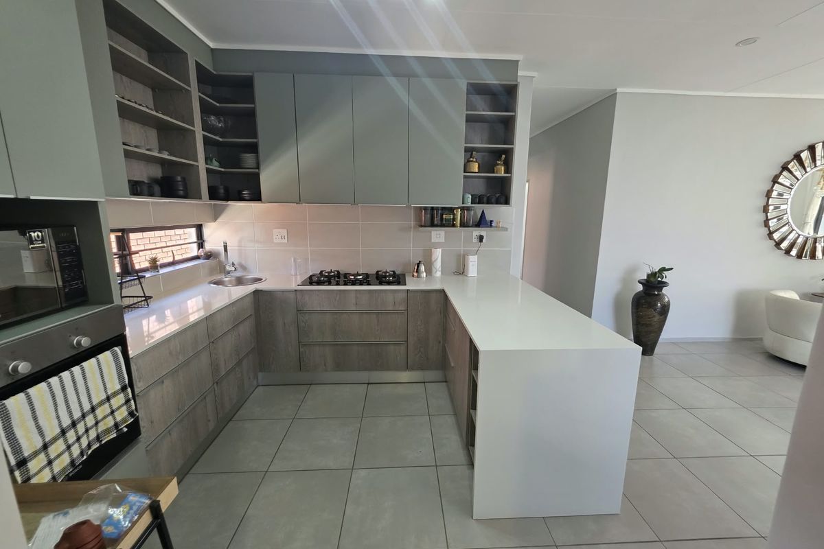 Modern kitchen featuring sleek two-tone cabinetry, stone countertops, a gas hob, built-in oven, and a functional breakfast bar with tiled flooring.