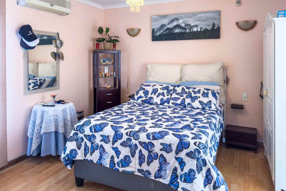 A cozy bedroom featuring light wood-look flooring, a wall-mounted air conditioning unit, and a central light fixture.
