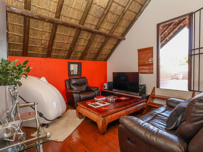 Living room featuring a vaulted thatched ceiling with exposed timber rafters, hardwood flooring, and direct access to an outdoor balcony area.