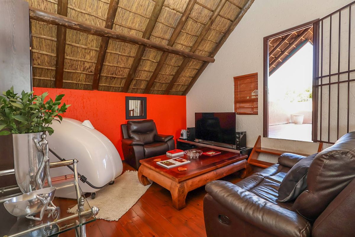 Living room featuring a vaulted thatched ceiling with exposed timber rafters, hardwood flooring, and direct access to an outdoor balcony area.