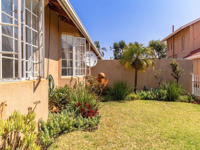 A private rear garden area featuring a lawn, established landscaping, boundary walls, and metal fencing, providing a quiet outdoor space for the townhouse.