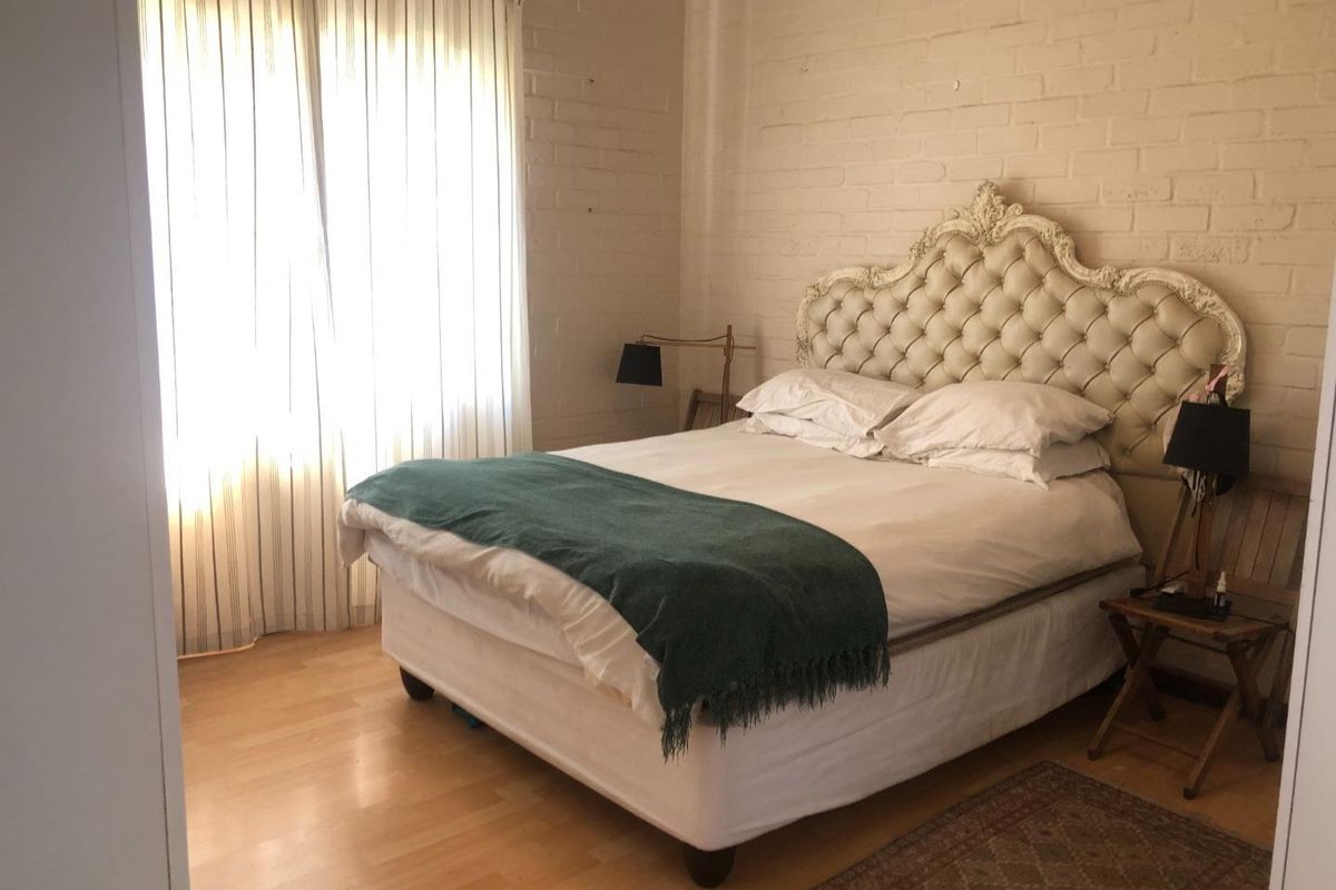 A bedroom featuring painted brick walls, laminate flooring, and large windows with curtains.