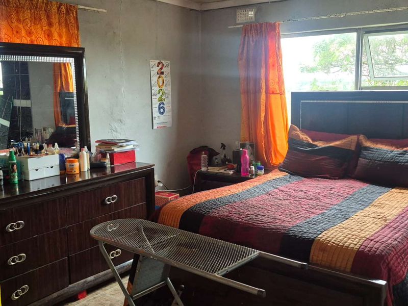 A bedroom featuring a large window with aluminium frames, showing signs of wear on the walls requiring maintenance and cosmetic updates.