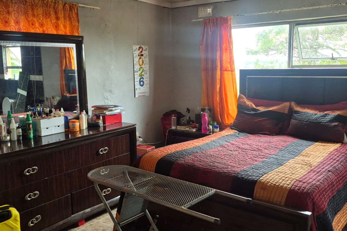A bedroom featuring a large window with aluminium frames, showing signs of wear on the walls requiring maintenance and cosmetic updates.