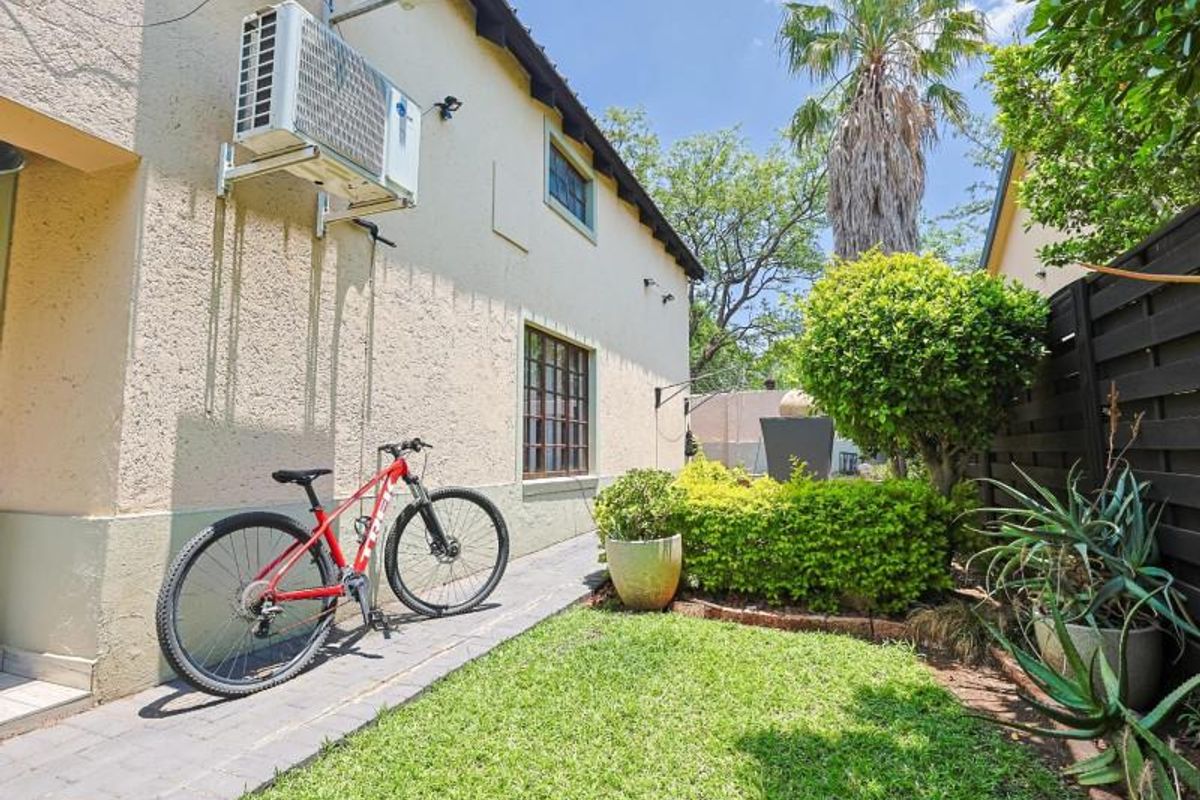 A well-maintained rear garden area featuring a paved walkway, established landscaping, and a wall-mounted air conditioning unit.