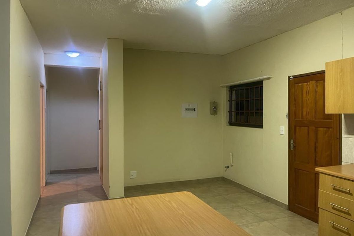 An interior view of an open plan living area featuring tiled flooring, a wooden door, and access to a hallway.