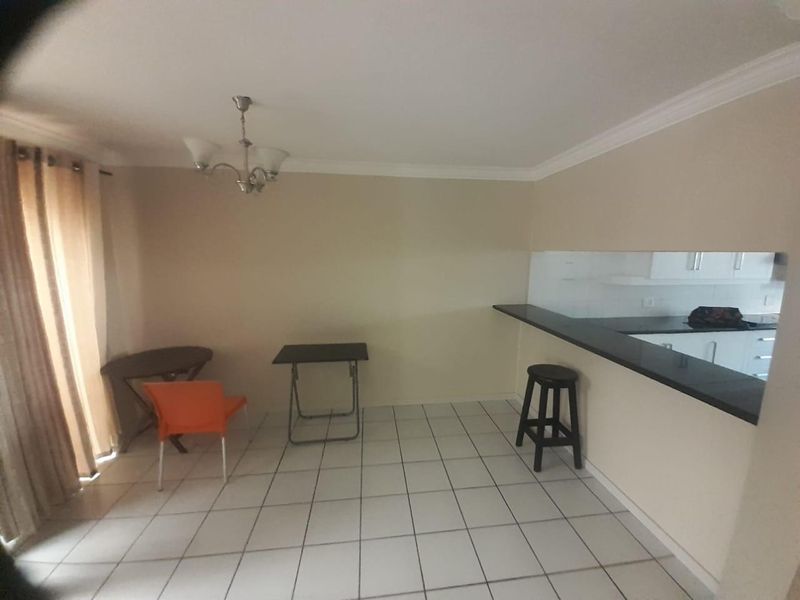 Open plan living and dining area featuring tiled flooring, a breakfast bar overlooking the kitchen, and neutral wall finishes.