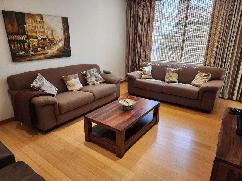 A comfortable living room featuring light-toned laminate flooring and large windows dressed with curtains and blinds.