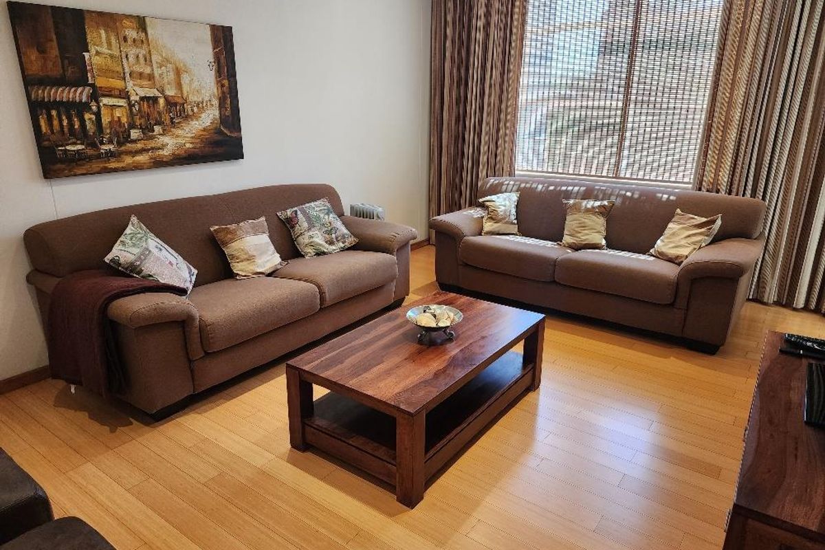 A comfortable living room featuring light-toned laminate flooring and large windows dressed with curtains and blinds.