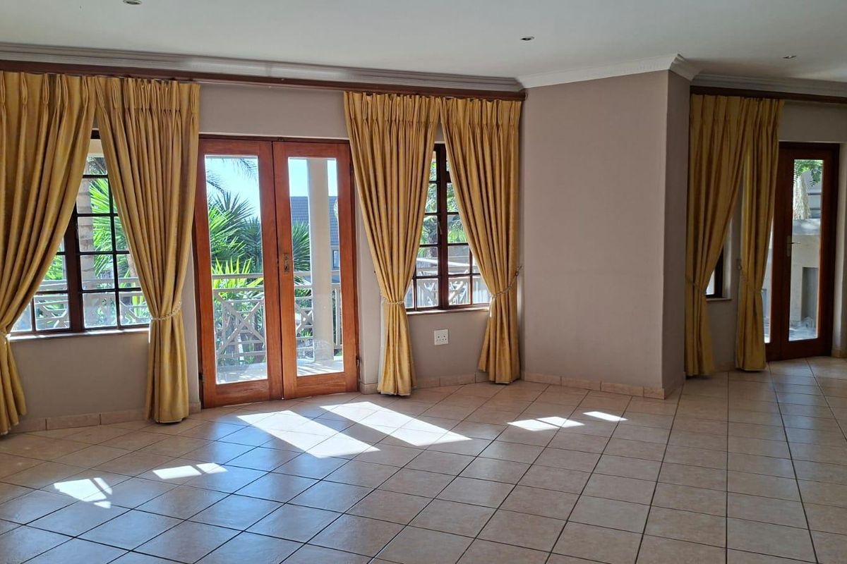 Spacious living area featuring neutral tiled flooring, recessed lighting, and wooden framed glass doors providing access to an outdoor space.