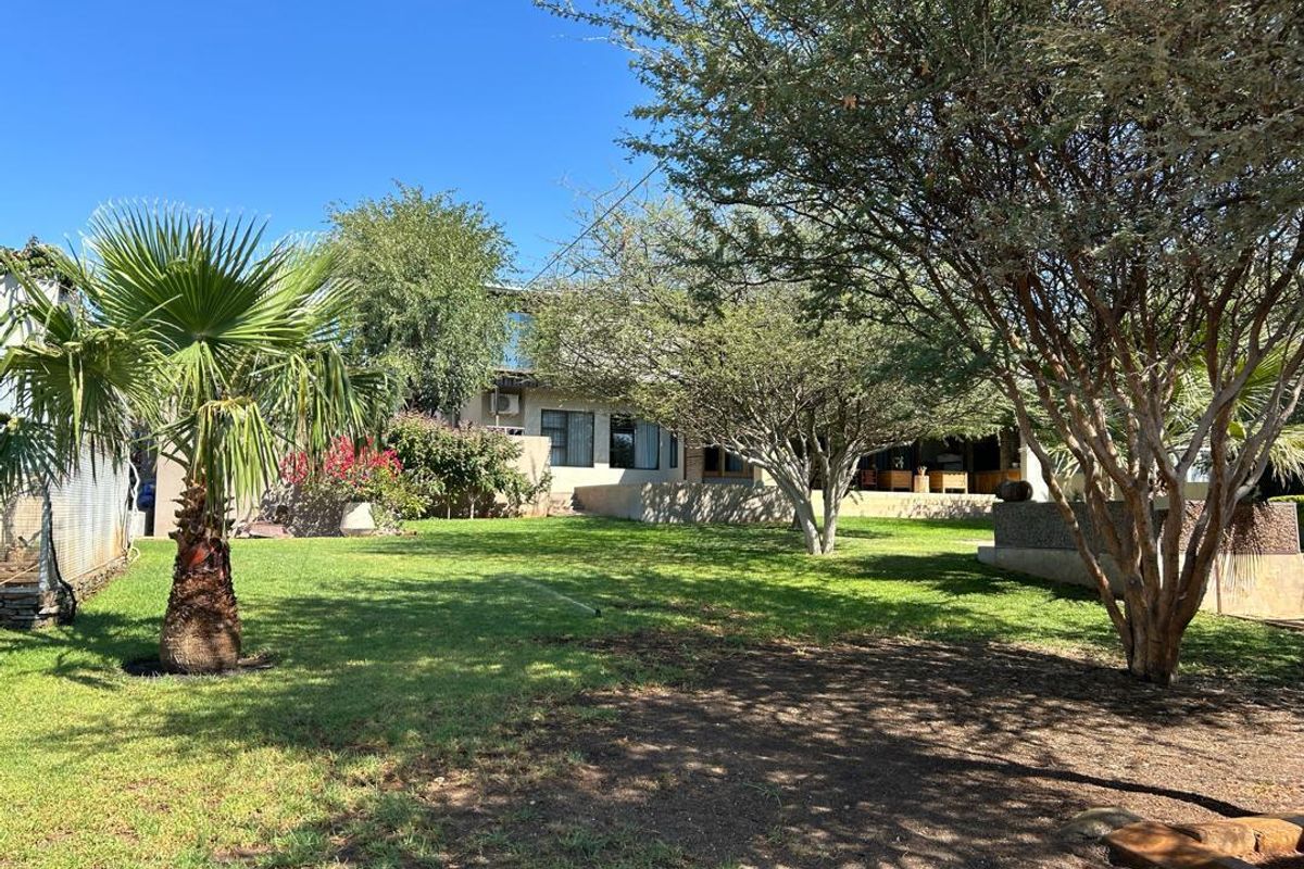 A spacious rear garden featuring mature trees, a well-maintained lawn, and a view of the property's rear elevation and patio area.