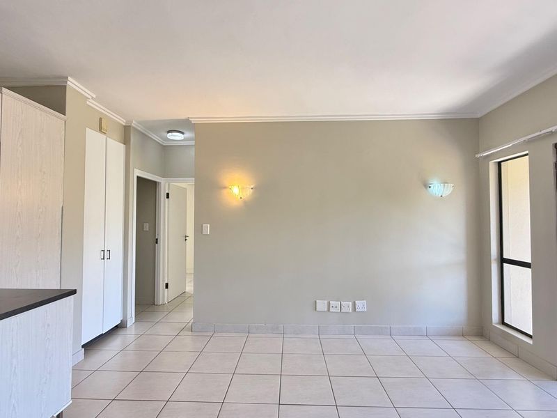 An open-plan living area featuring neutral tiled flooring, built-in storage cupboards, wall sconces, and a security gate leading to an outdoor space.