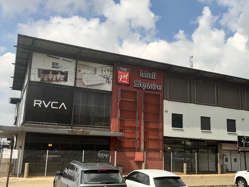 Front elevation of The Mall Square retail building featuring modern commercial architecture, prominent signage, and an adjacent paved parking area.