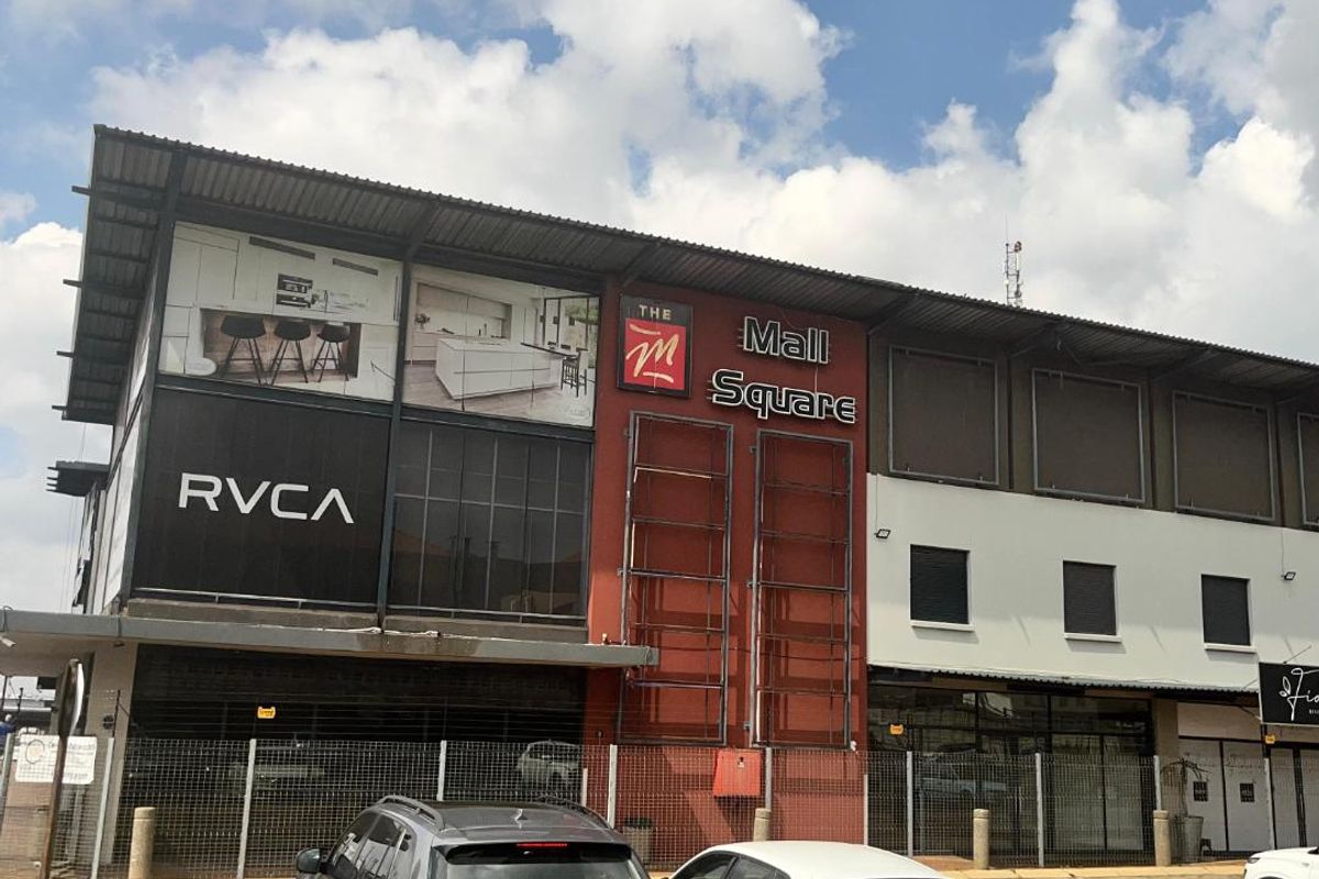 Front elevation of The Mall Square retail building featuring modern commercial architecture, prominent signage, and an adjacent paved parking area.
