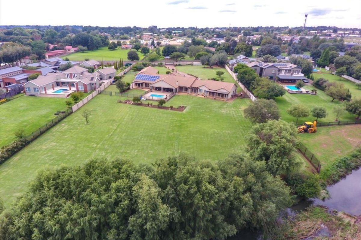 Aerial view of a large residential property featuring a spacious lawn, swimming pool, and solar panel installation on the roof.
