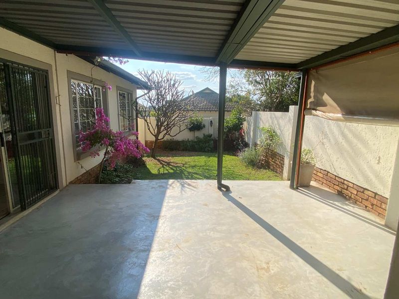 A covered patio area featuring concrete flooring, overlooking a private garden with established trees and a secure boundary wall.