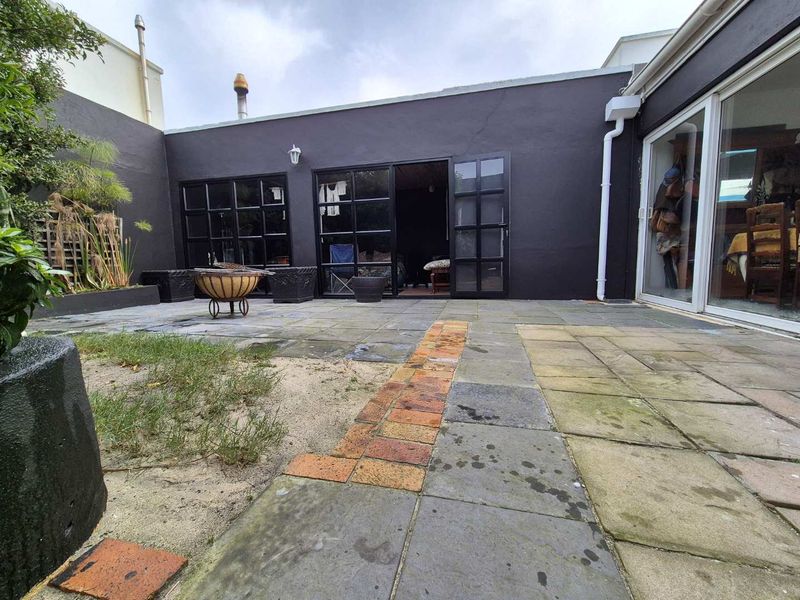 A rear courtyard featuring paved surfaces, brick accents, and black-framed glass doors providing access to the interior living space.