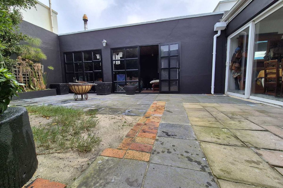 A rear courtyard featuring paved surfaces, brick accents, and black-framed glass doors providing access to the interior living space.
