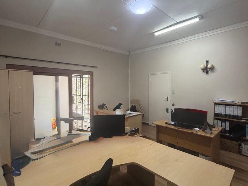 A functional office space featuring laminate flooring, fluorescent lighting, and a sliding glass door with security gate access.