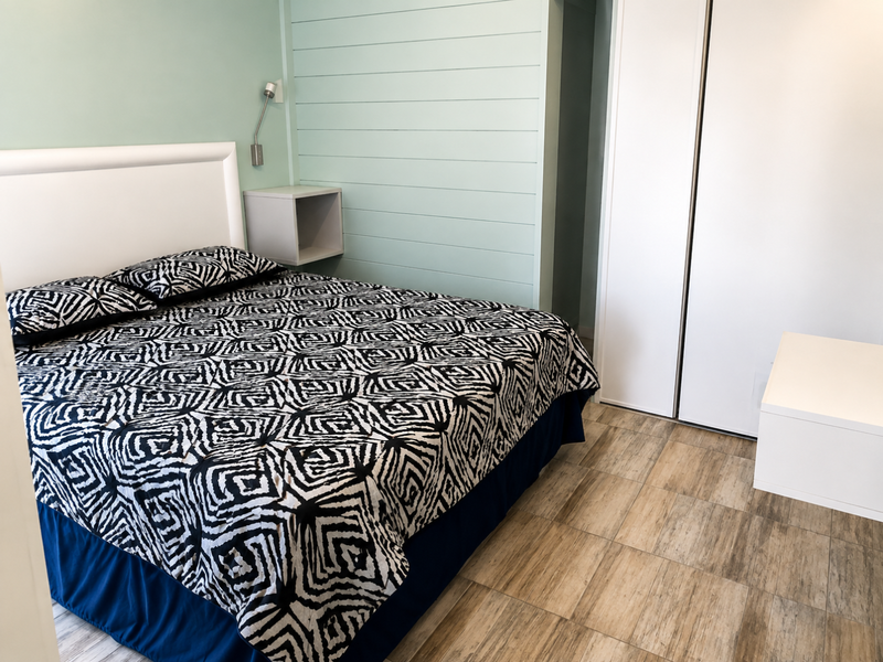 A well-maintained bedroom featuring timber-look floor tiles, horizontal wall paneling, a built-in wardrobe, and a modern wall-mounted reading light.