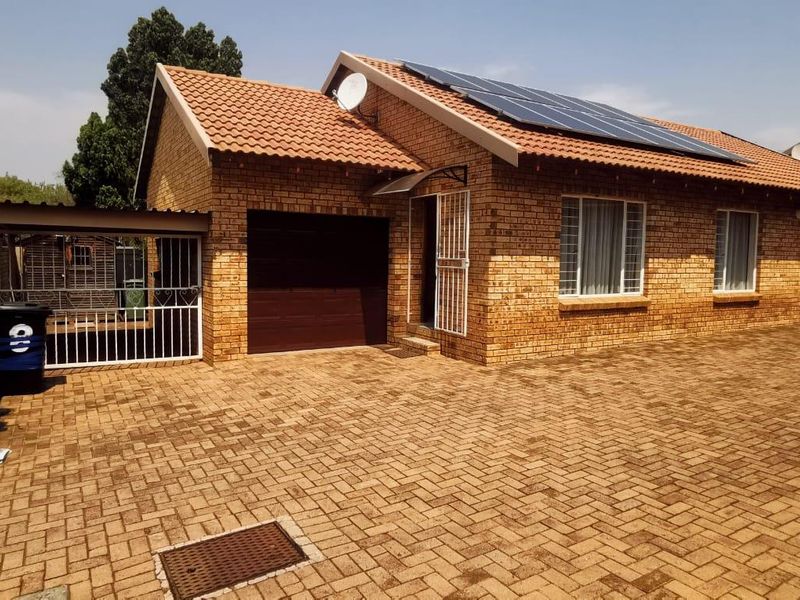 Front view of a facebrick cluster home featuring a paved driveway, single garage, and roof-mounted solar panels.