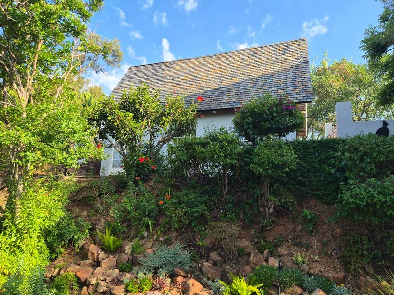 A view of the cottage rear elevation featuring a traditional slate roof, set against a lush, terraced garden with stone retaining walls.
