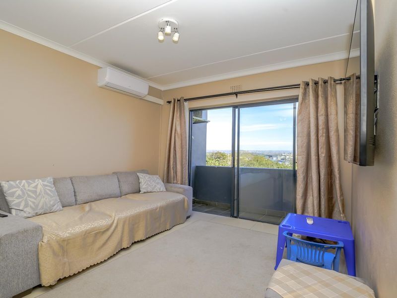 A living room featuring tiled flooring, an air conditioning unit, and a sliding glass door providing access to a balcony with a view.