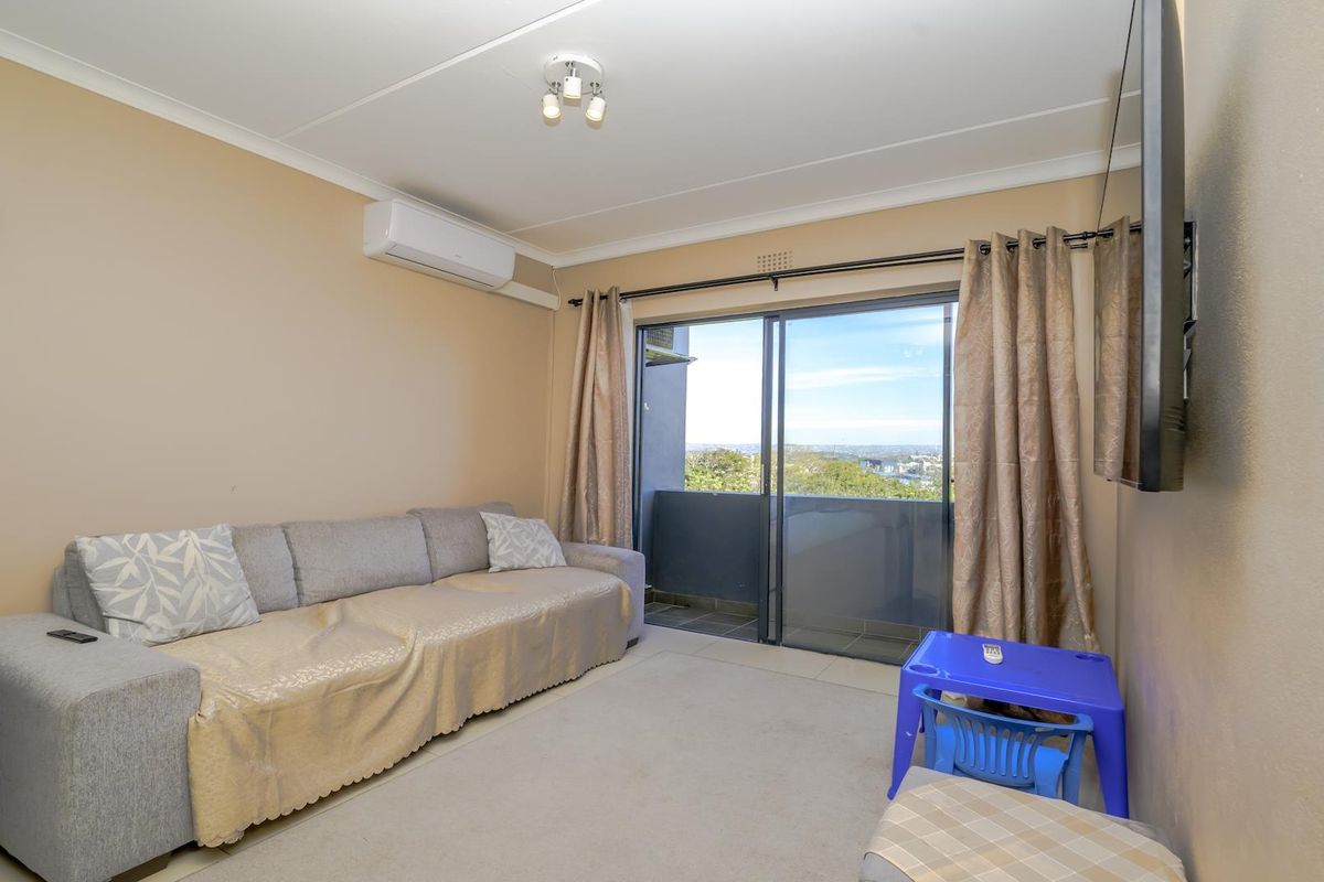 A living room featuring tiled flooring, an air conditioning unit, and a sliding glass door providing access to a balcony with a view.