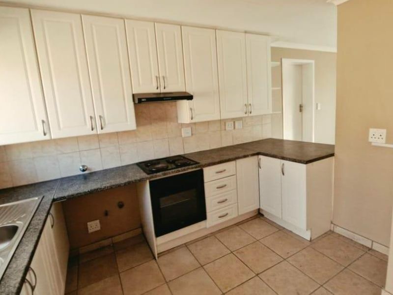 A functional kitchen featuring white cabinetry, dark laminate countertops, built-in oven with hob, and tiled flooring, offering a clean canvas for updates.