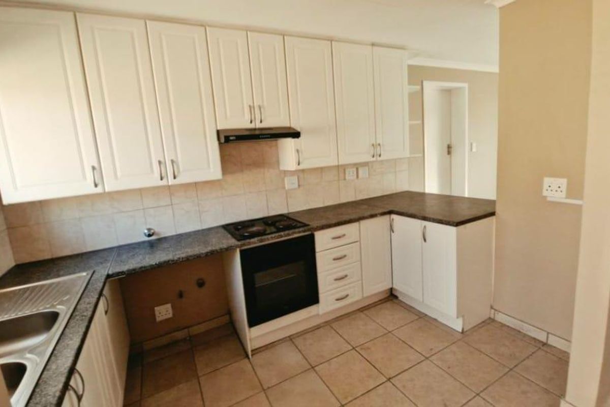 A functional kitchen featuring white cabinetry, dark laminate countertops, built-in oven with hob, and tiled flooring, offering a clean canvas for updates.