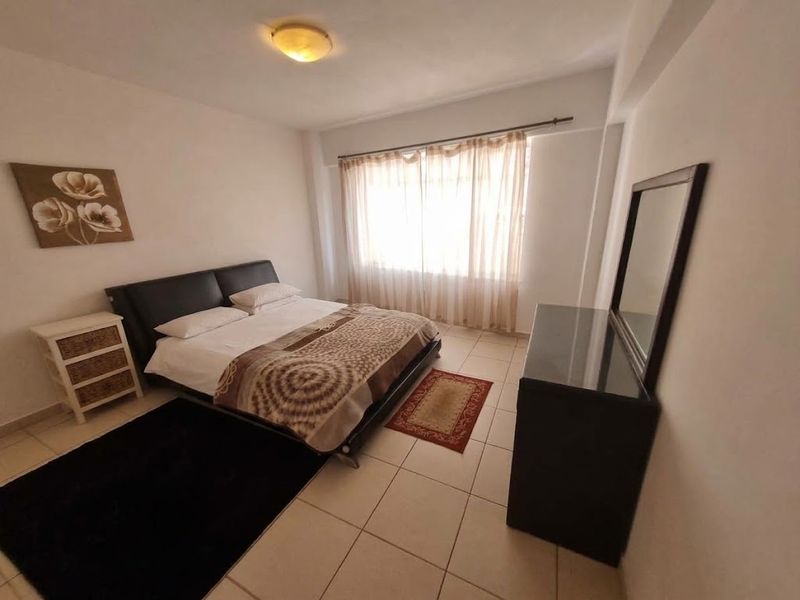 A functional bedroom featuring tiled flooring, neutral walls, and a large window with curtains, providing a bright and comfortable living space.
