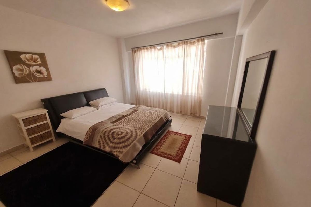 A functional bedroom featuring tiled flooring, neutral walls, and a large window with curtains, providing a bright and comfortable living space.