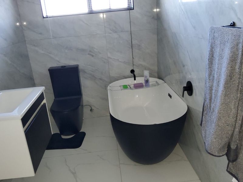 Modern bathroom featuring a sleek freestanding bathtub, wall-mounted basin with vanity, and contemporary black matte fixtures against elegant marble-look tiled walls.