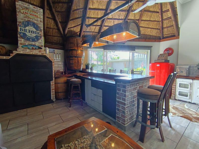 A rustic-style bar area featuring a built-in brick counter, a traditional thatched roof, and a built-in fireplace, opening out to the garden.