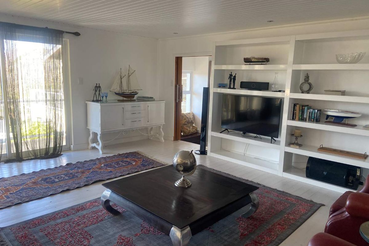 A bright living room featuring built-in floor-to-ceiling shelving, recessed lighting, and sliding glass doors providing access to the outdoor area.