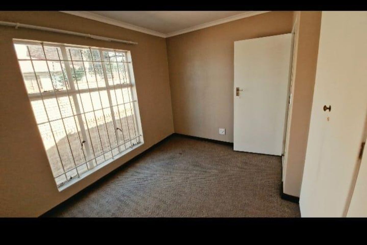 An empty bedroom featuring carpeted flooring, built-in cupboards, and a window fitted with security bars.