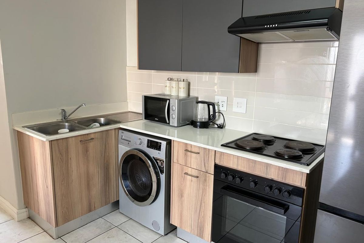 Modern kitchen featuring wood-finish cabinetry, contrasting grey upper cabinets, integrated electric hob, oven, extractor fan, and a stainless steel sink with tiled backsplash.