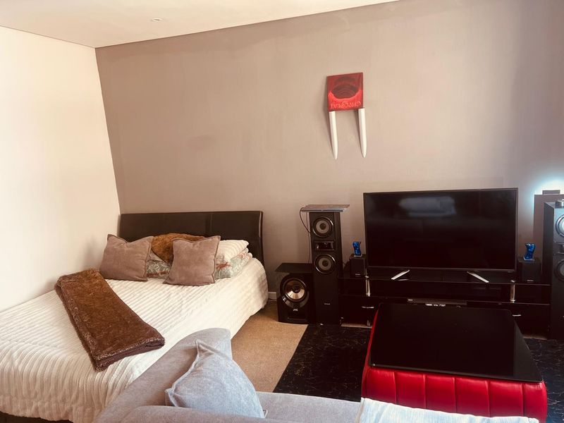 A bedroom space featuring neutral wall tones and carpeted flooring, currently utilized as a multi-purpose living and sleeping area.