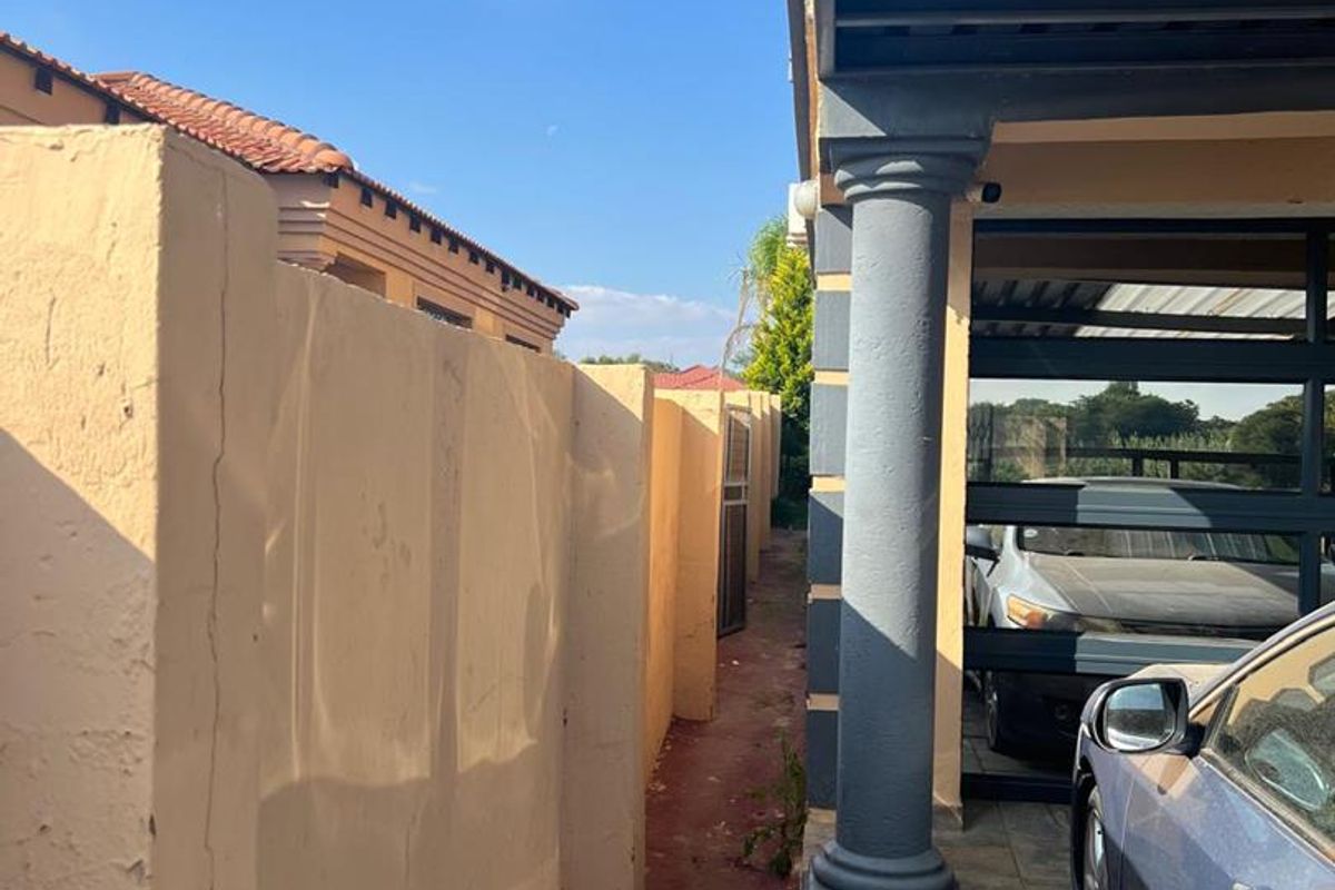 Side passage of the property featuring a boundary wall, paved walkway, and a covered carport area with a structural pillar.
