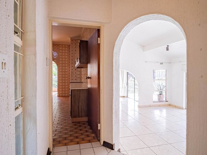 A view from the hallway looking into an open-plan living area and kitchen, featuring arched architectural details and neutral tiled flooring throughout.