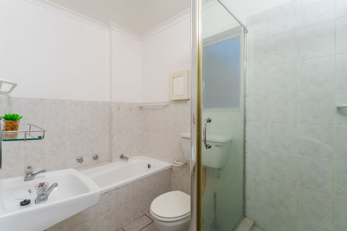 A functional bathroom featuring a combined bathtub and shower enclosure, pedestal basin, and toilet with neutral wall tiling.