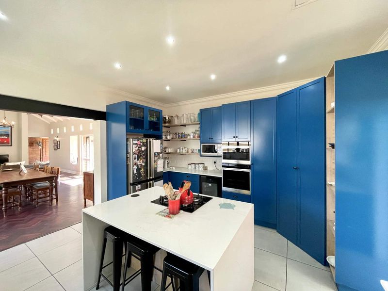Modern kitchen featuring vibrant blue cabinetry, a central island with stone countertops, built-in appliances, and recessed lighting, seamlessly flowing into the adjacent dining area.