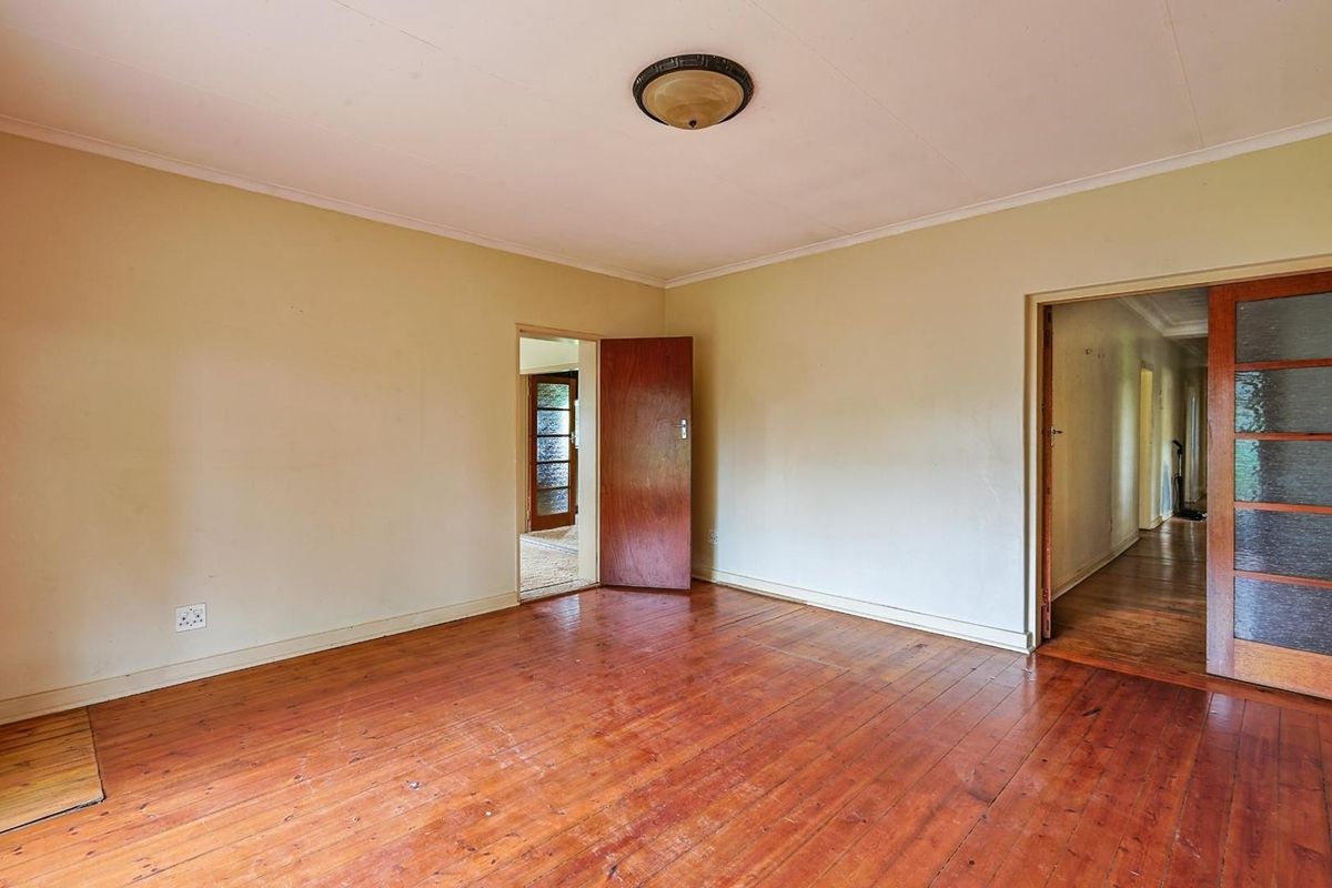 An empty room featuring original timber flooring, a central ceiling light fixture, and wooden door frames leading to adjacent spaces.