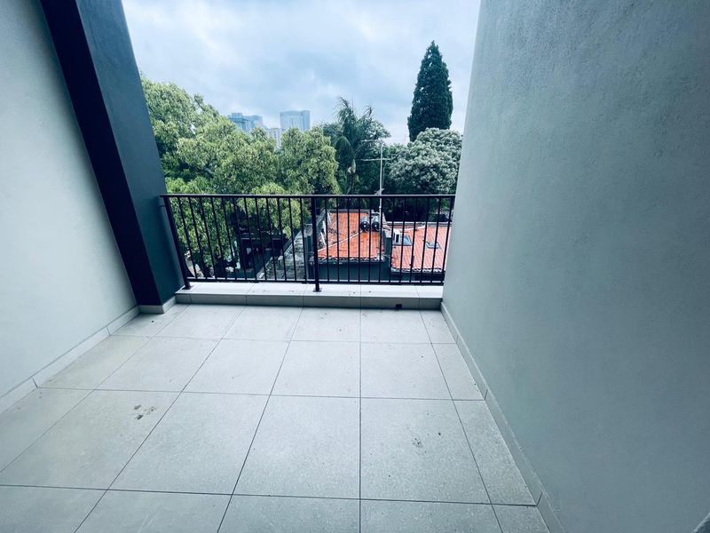 A clean, covered balcony featuring tiled flooring and a metal balustrade, offering an elevated view of the surrounding trees and neighborhood.